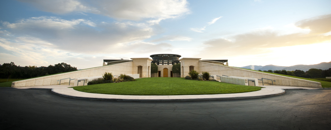 Moderne Architektur vor bewölktem Himmel, umgeben von grünem Rasen und gepflasterter Straße.